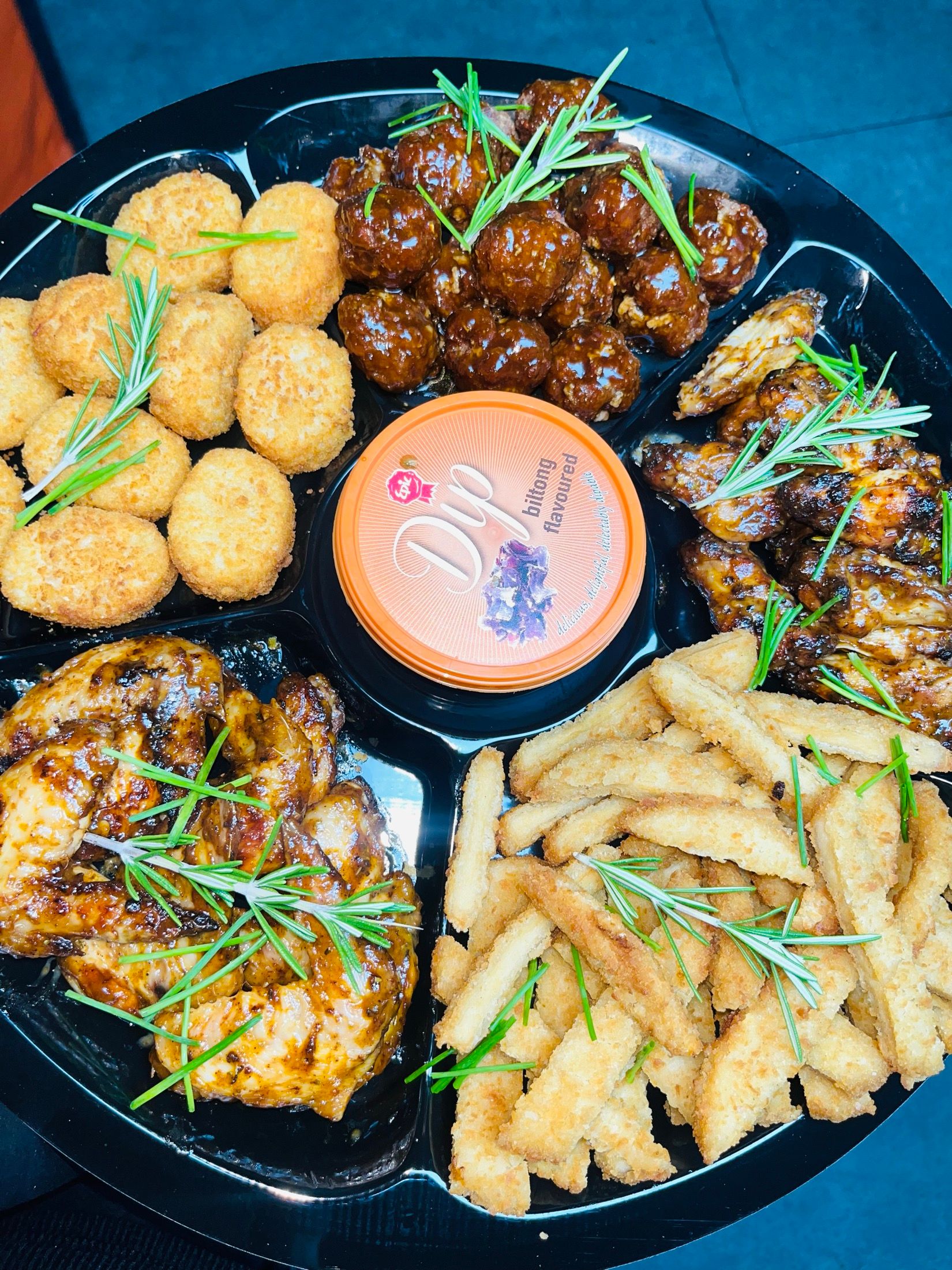 A Black Diamond catering platter: grilled chicken pieces and wings, crumbed jalapeño poppers, potato wedges and a tub of dip, garnished with rosemary.