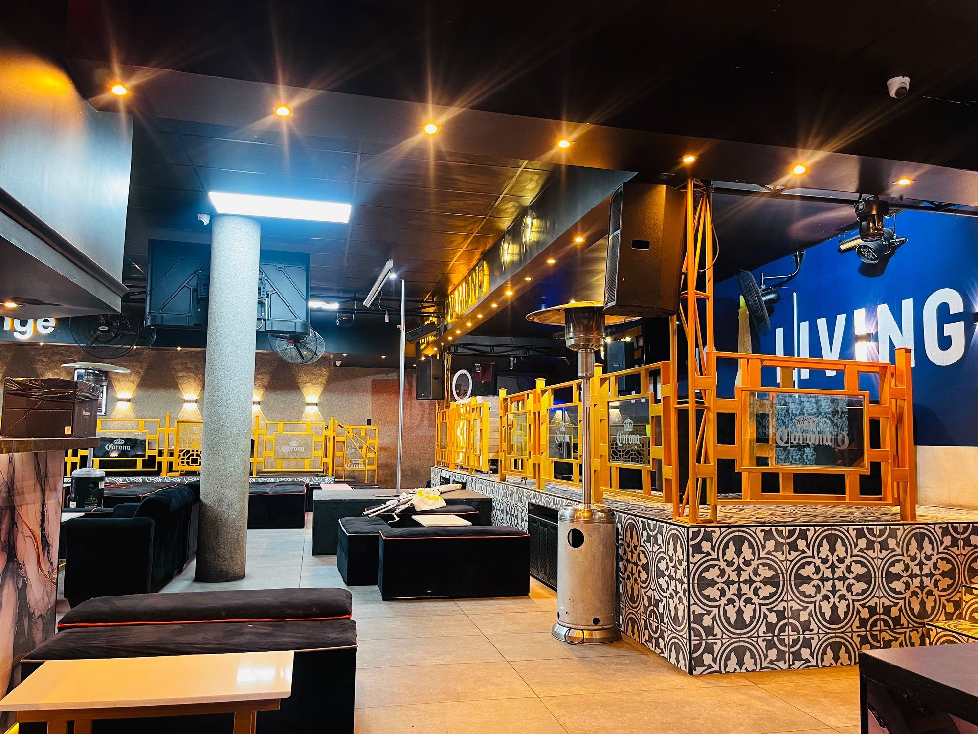 A lounge area with a patterned tiled bar station, a gas heater, a gold screen divider and dark seating, with a blue LIVING sign glowing on the far wall.