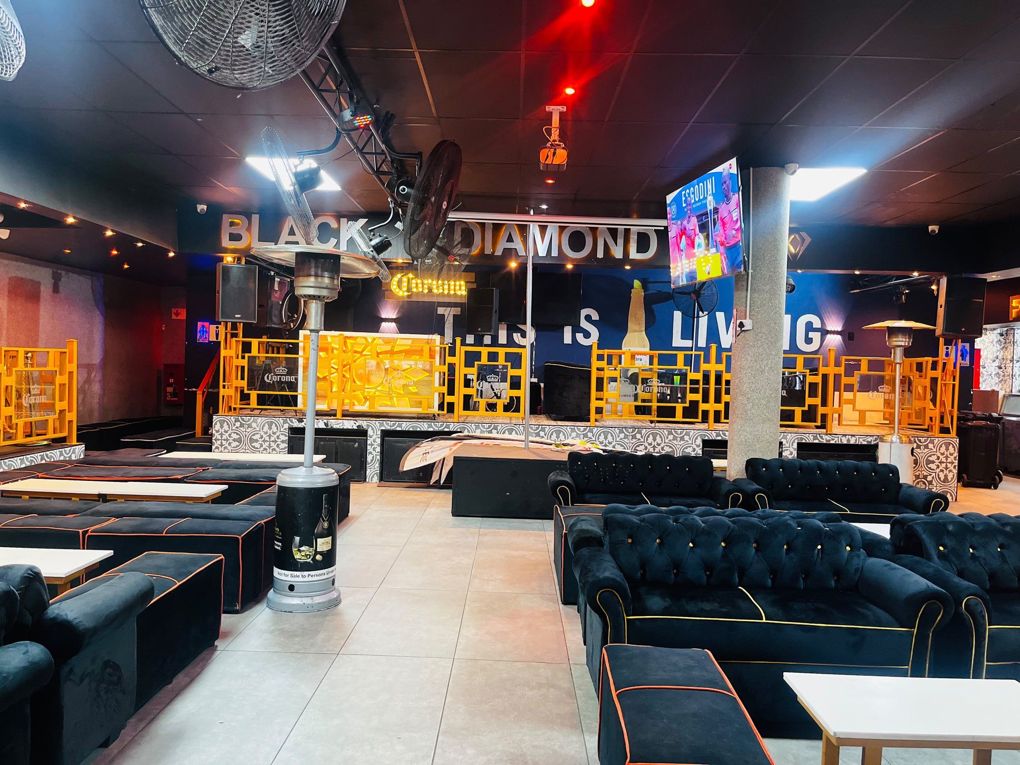 Low velvet benches and white tables on patterned tiling, with a gas heater and a raised platform edged by patterned floor tiles behind.