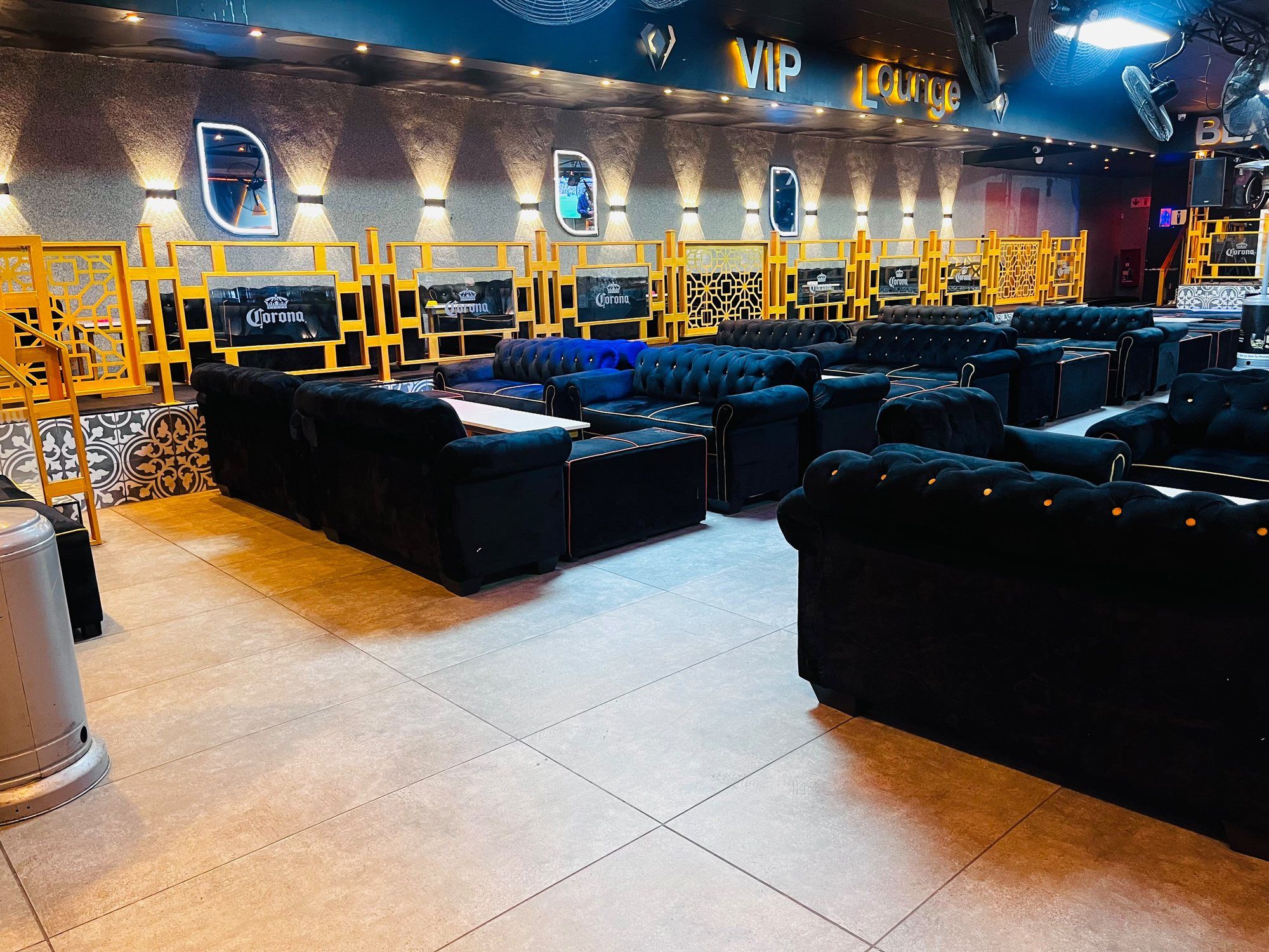 The VIP lounge at Black Diamond: an illuminated VIP Lounge sign in gold above a stone-clad wall washed by uplights, a gold balustrade edging the raised area, and rows of black buttoned velvet couches with low tables.